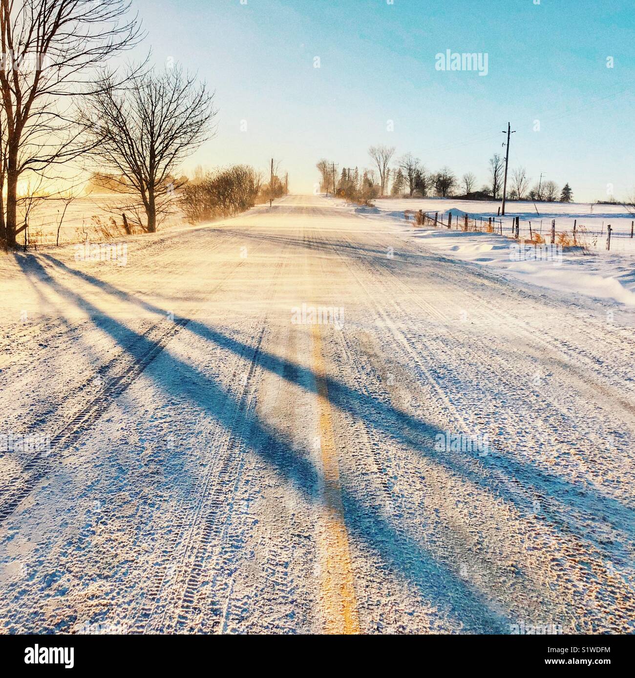 Ländliche Straße mit der gelben Linie im Schnee bedeckt mit Schnee Wind weht über bei Sonnenuntergang Stockfoto