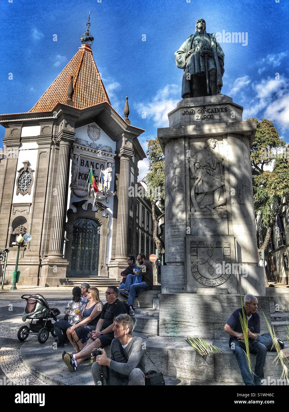Leute sitzen am Sockel der Statue von Zorca, vor dem ikonischen Bank von Portugal auf der Av. Arriaga, Funchal, Madeira, Portugal Stockfoto