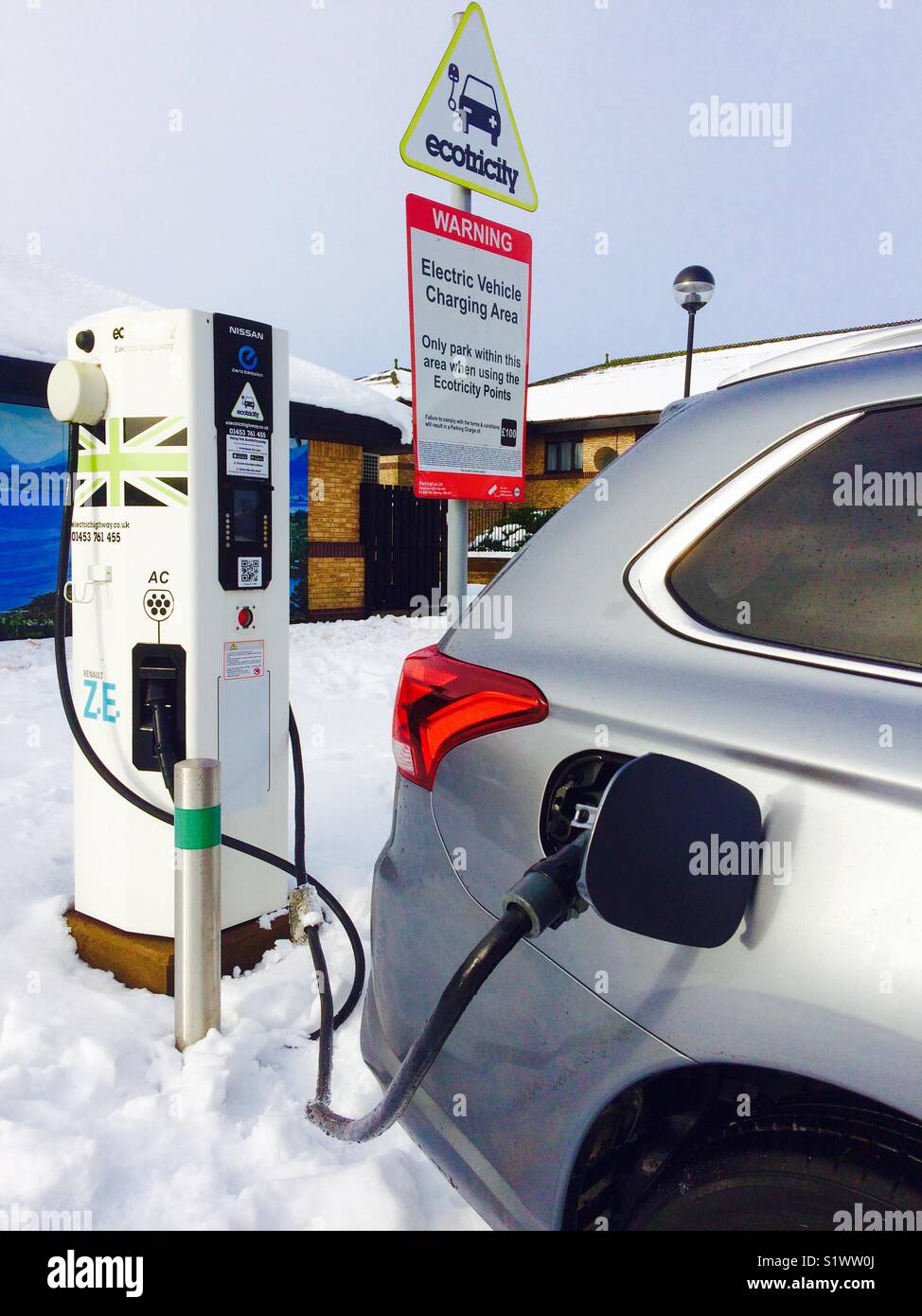 PHEV für Elektrofahrzeuge Plug-in Hybrid-Fahrzeug Mitsubishi Outlander PHEV an eine Gridserve EV Ladestation CHAdeMO-Kabel im Schnee angeschlossen - Smartphone-aufgenommenes Stockfoto