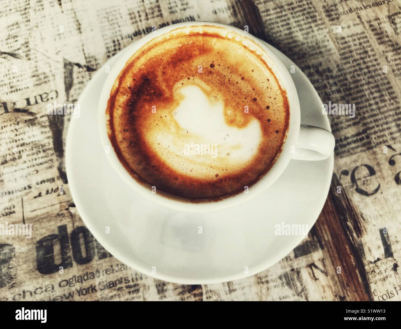 Cappuccino, auf einer Tischplatte mit portugiesischen Zeitungen eingerichtet. Madeira, Portugal - Smartphone-aufgenommenes Stockfoto