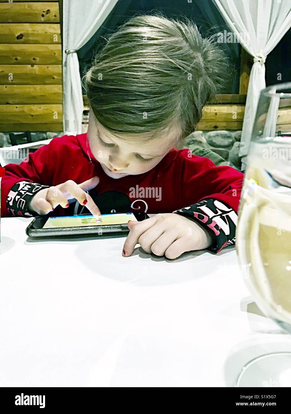 Kinder spielen auf dem Telefon zum Abendessen in einem Restaurant Stockfoto