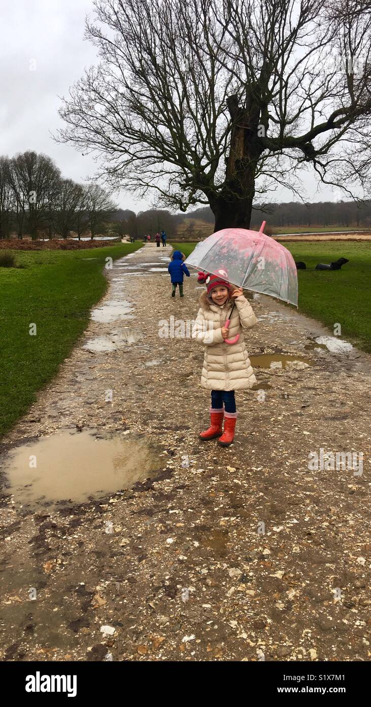 Kinder wandern in Richmond Park mit Regenschirm und Gummistiefel, den Pfützen auszuweichen. Stockfoto