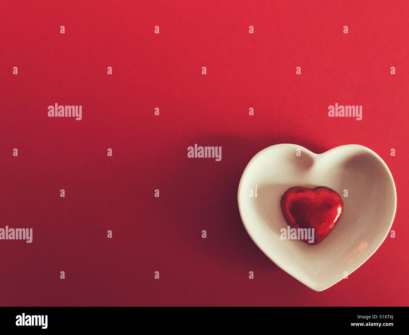 Valentinstag, Rot Schokolade Herz in einem weißen Herzförmige Schale auf rotem Hintergrund mit Kopie Raum - Smartphone-aufgenommenes Stockfoto