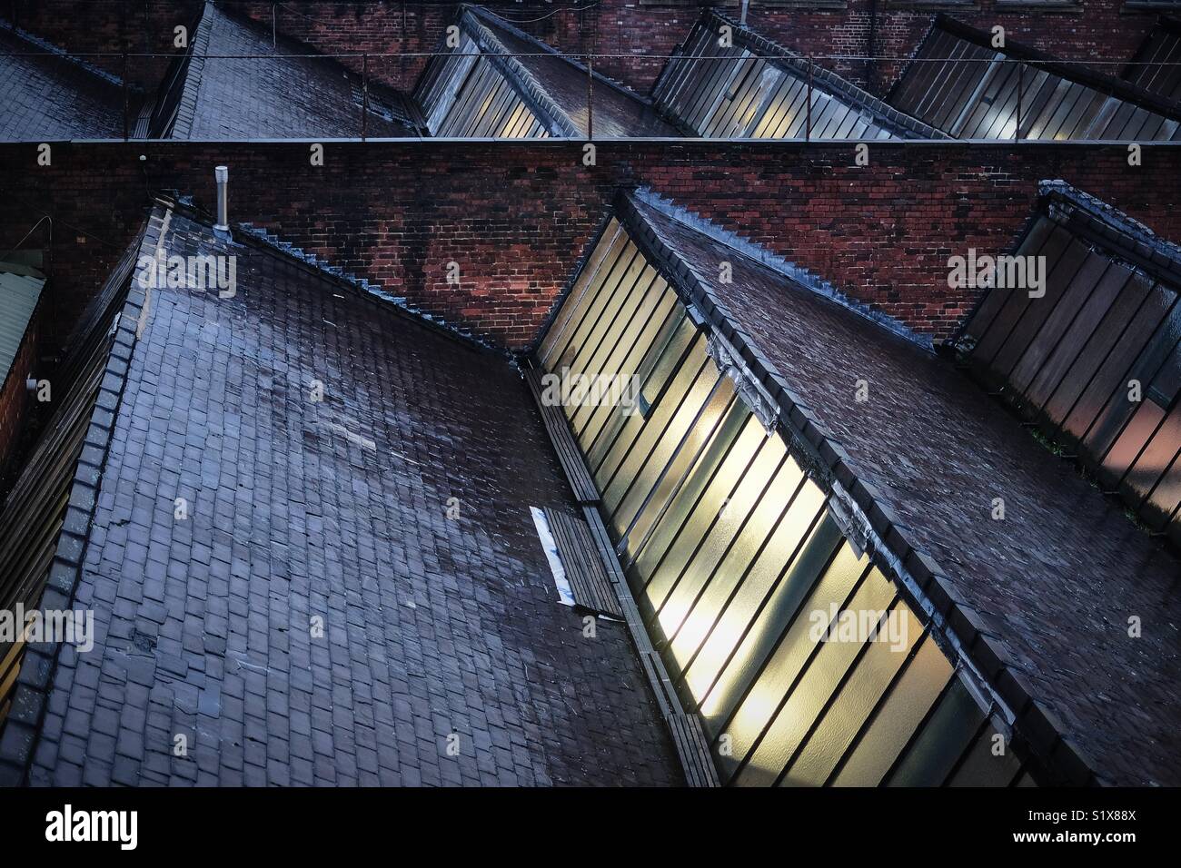 Nasse Fliesen und Mauerwerk auf dem Dach einer Fabrik im Norden von England mit Licht scheint durch die Glasfenster. Stockfoto