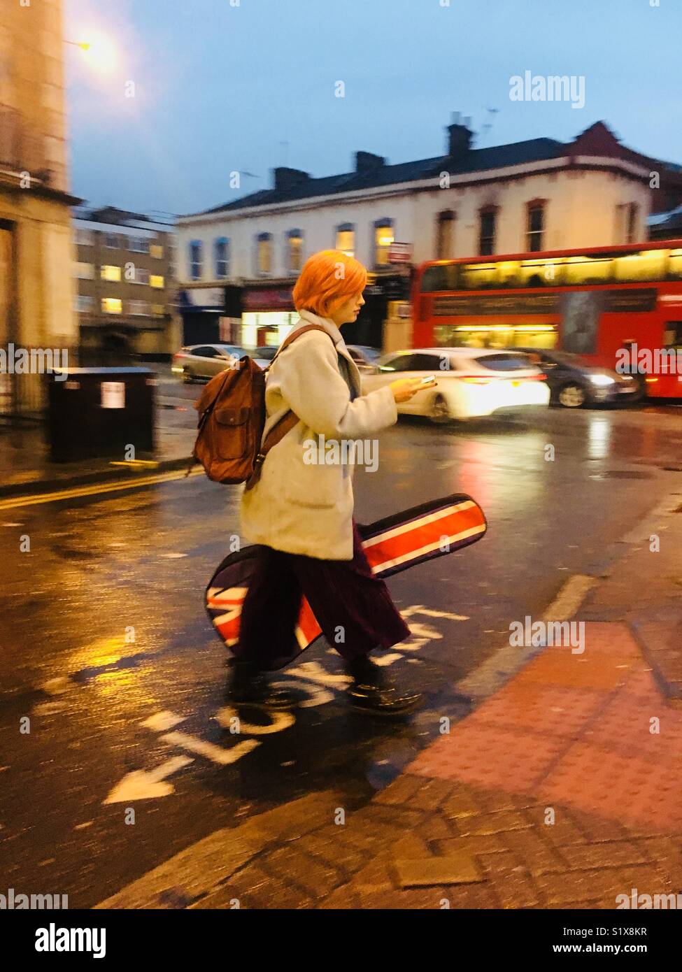 Rothaarige Frau Kreuzung an Fußgänger überqueren, als sie eine Gitarre mit britischer Flagge trägt - Smartphone-aufgenommenes Stockfoto