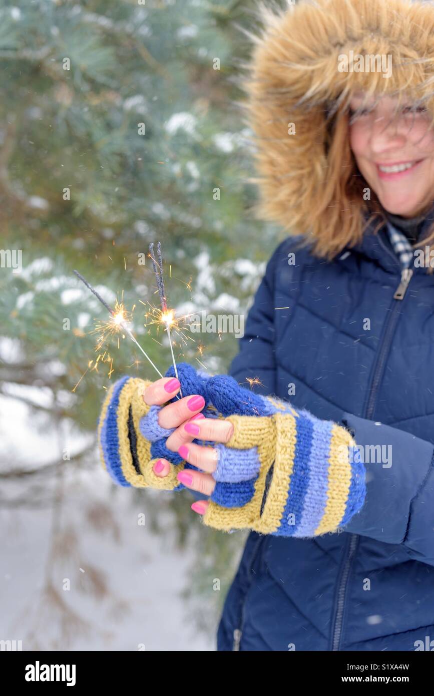 Lächelnde Frau in hellen Farben stricken Handschuhe holding Wunderkerzen im Schnee An einem kalten Wintertag Stockfoto