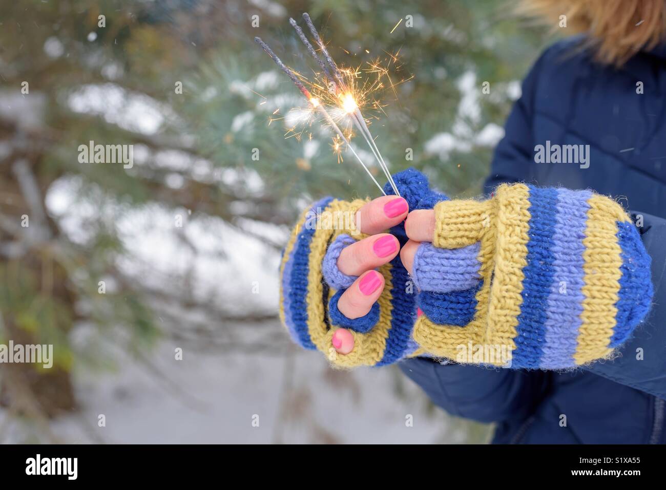 Frau in bunten Blau und Gelb stricken Handschuhe holding Wunderkerzen an einem Wintertag Stockfoto