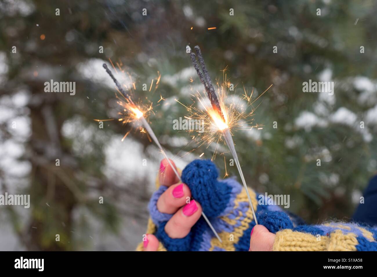 Nahaufnahme der Frau in bunte Gestrickte Handschuhe Holding lit Wunderkerzen an einer im Winter Festival Stockfoto