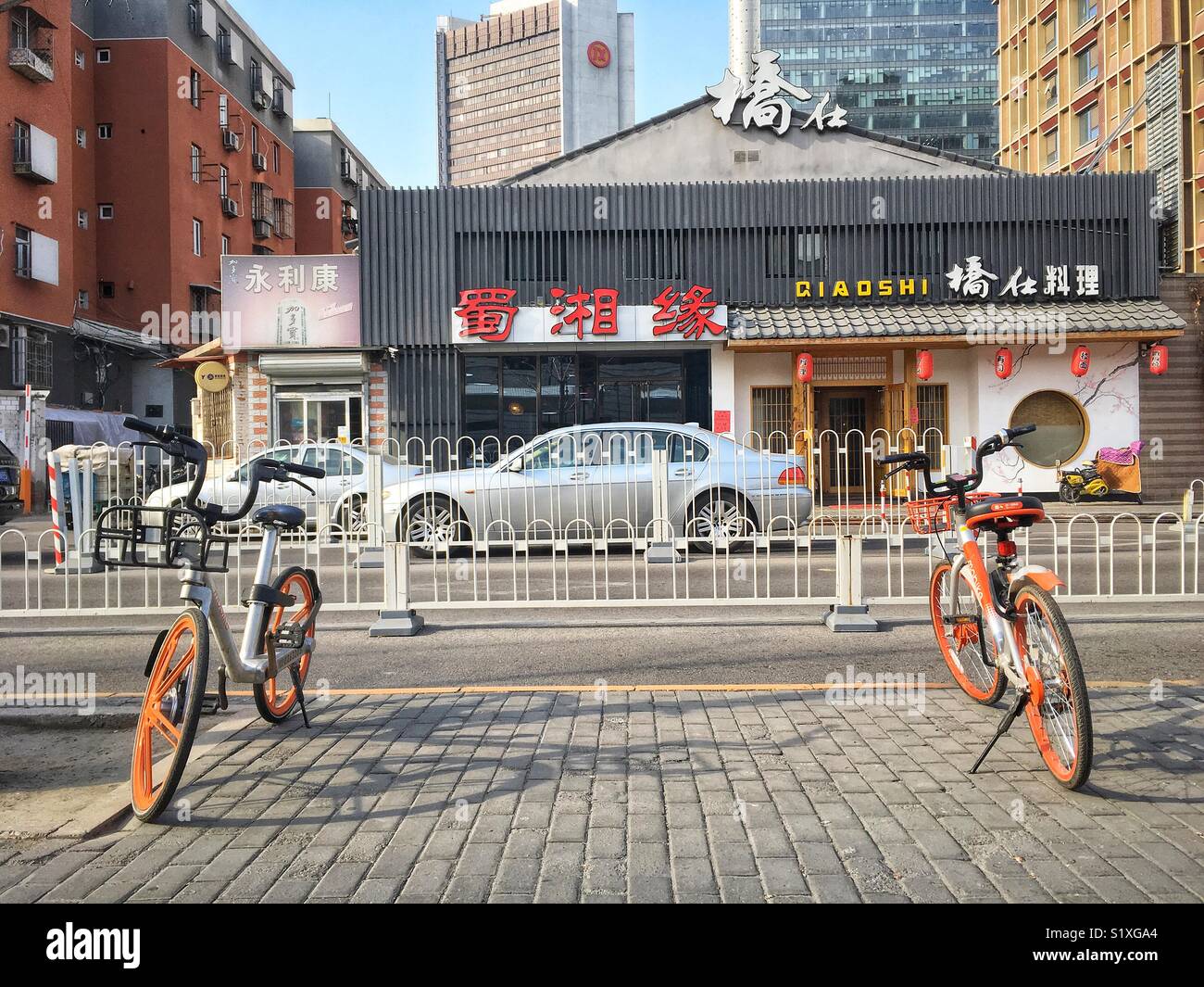 Peking, China Straße mit orange städtische Gemeinschafts-Fahrräder und Restaurants Zeichen in apposite Seite der Straße Stockfoto