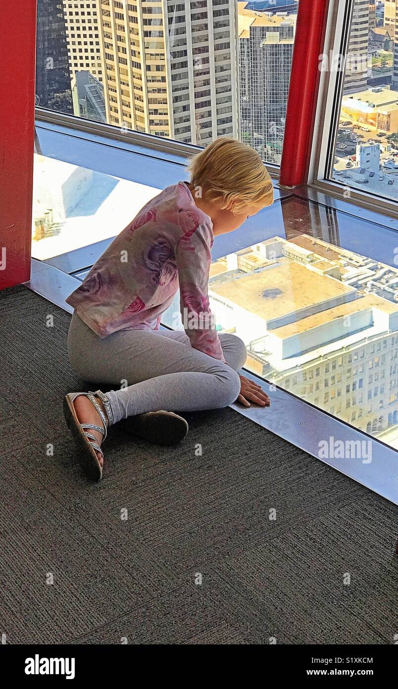 Ein Mädchen peers über den Glasboden des Calgary Tower. - Smartphone-aufgenommenes Stockfoto