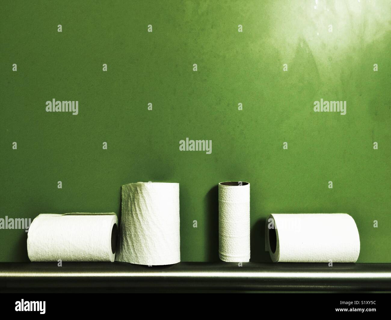 Halb fertig Toilettenpapierrollen auf Metall Geländer gegen grüne Wand Stockfoto