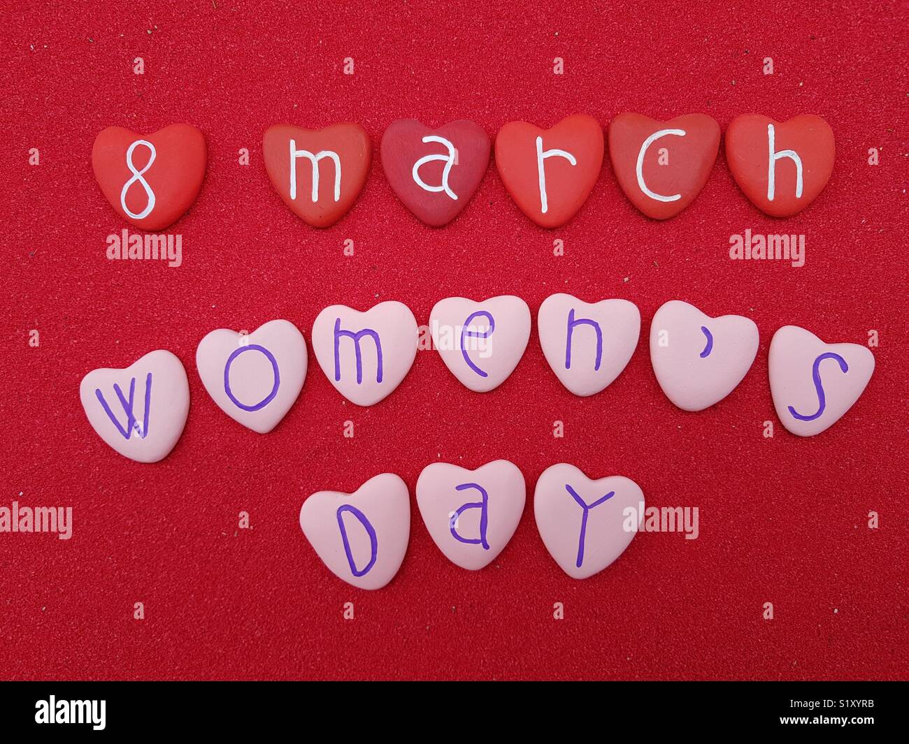 8. März, dem Tag der Frau mit roten und pinkfarbenen Herzen Steine über roten Sand Stockfoto