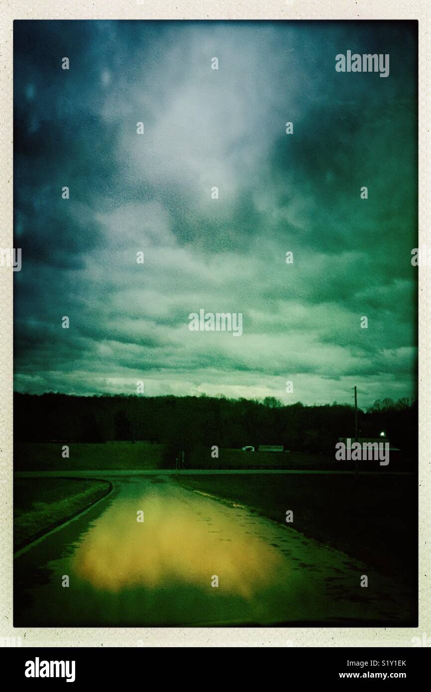 Scheinwerfer erhellen, eine Straße und dunkle Wolken rollen über der Landschaft erzeugen eine unheimliche Abend Szene. Stockfoto