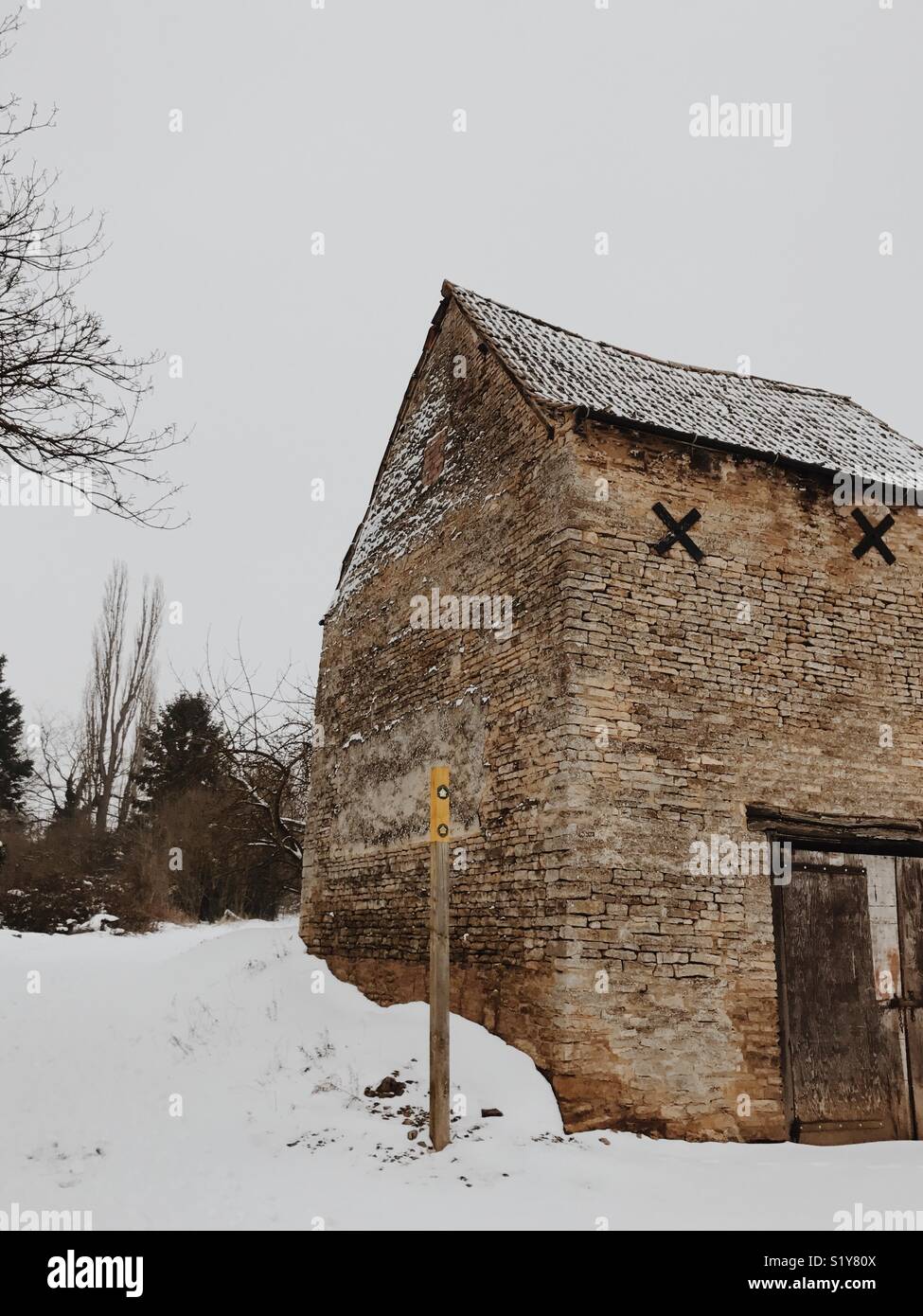 Alte Farm Barn in Englisch Dorf mit Schnee auf dem Boden und einem öffentlichen Fußweg Zeichen Stockfoto