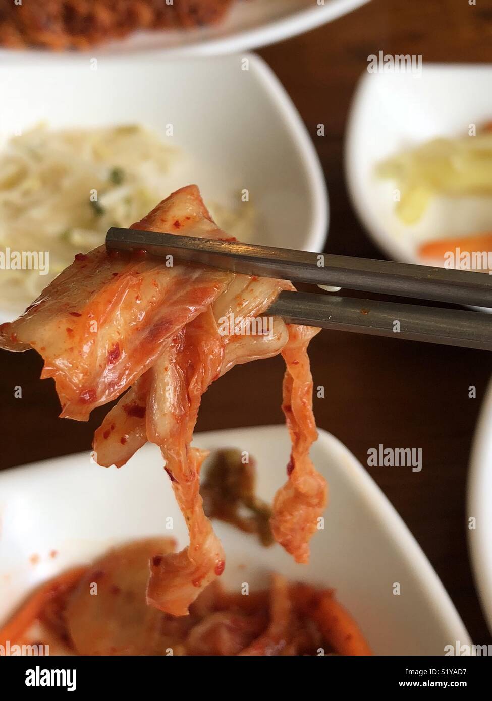 Halten Kimchi mit Stäbchen aus einem Seitenplatte Stockfoto