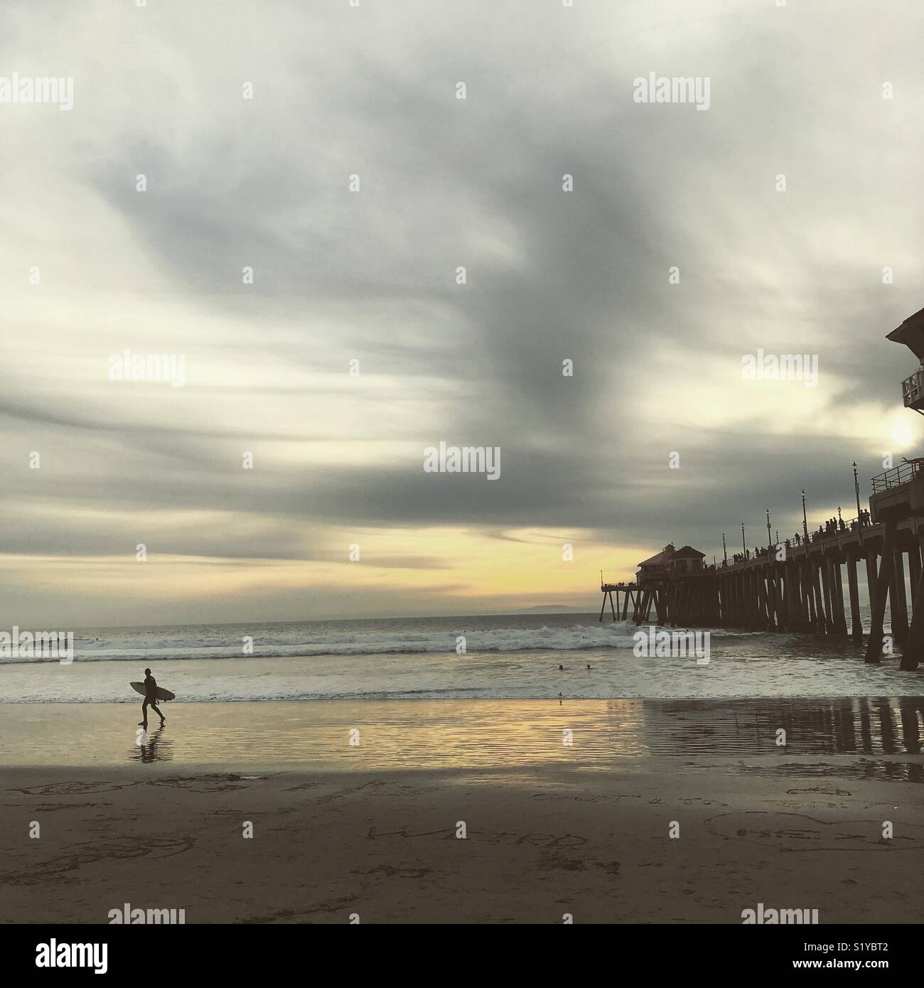 Ein surfer Spaziergänge über den weissen Sand Neben der Newport Beach Pier bei Sonnenuntergang Stockfoto