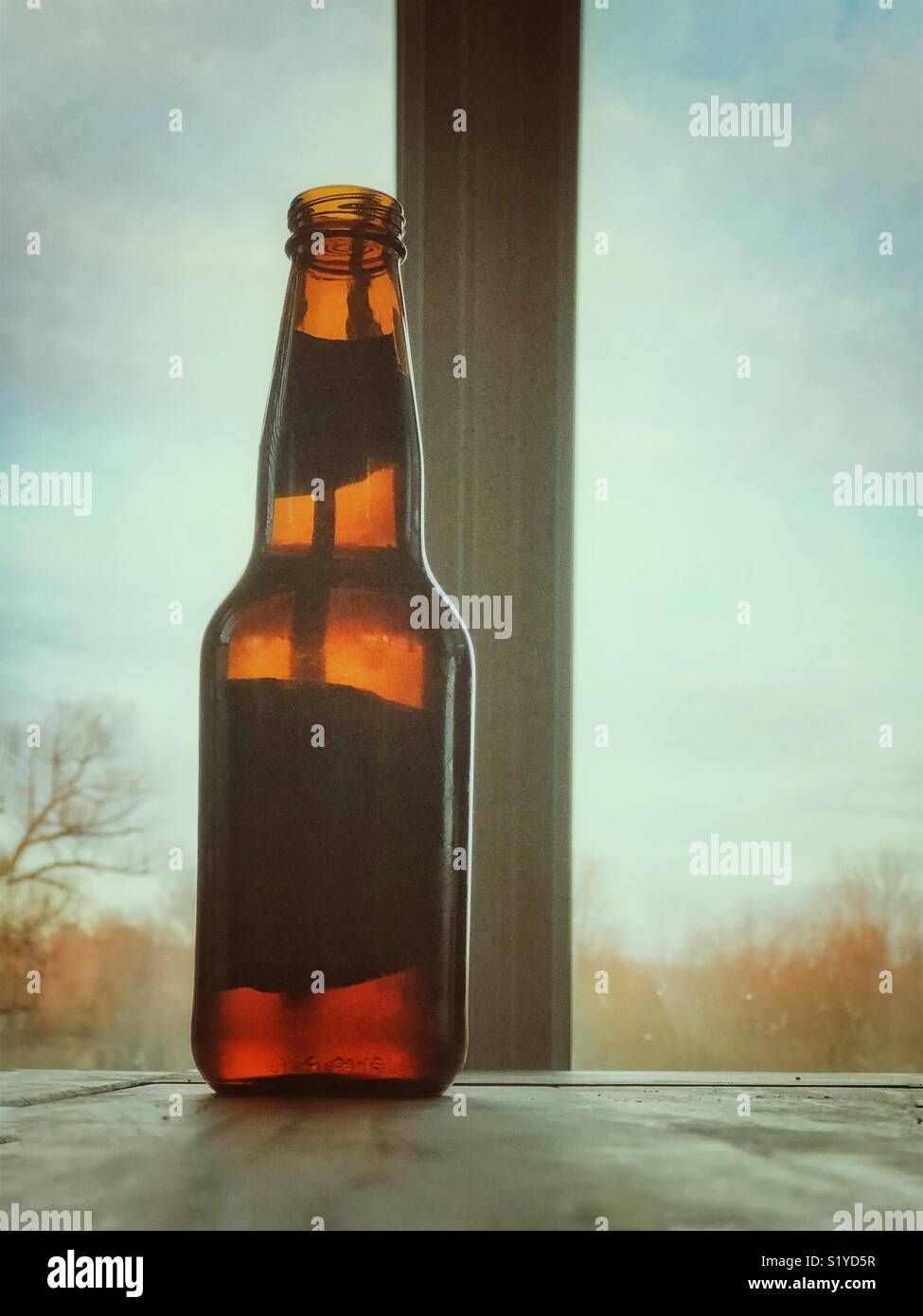 Flasche Bier in Braun Gelb Flasche auf hölzernen Tisch gegen Fenster Tageslicht Szene Silhouette - Smartphone-aufgenommenes Stockfoto