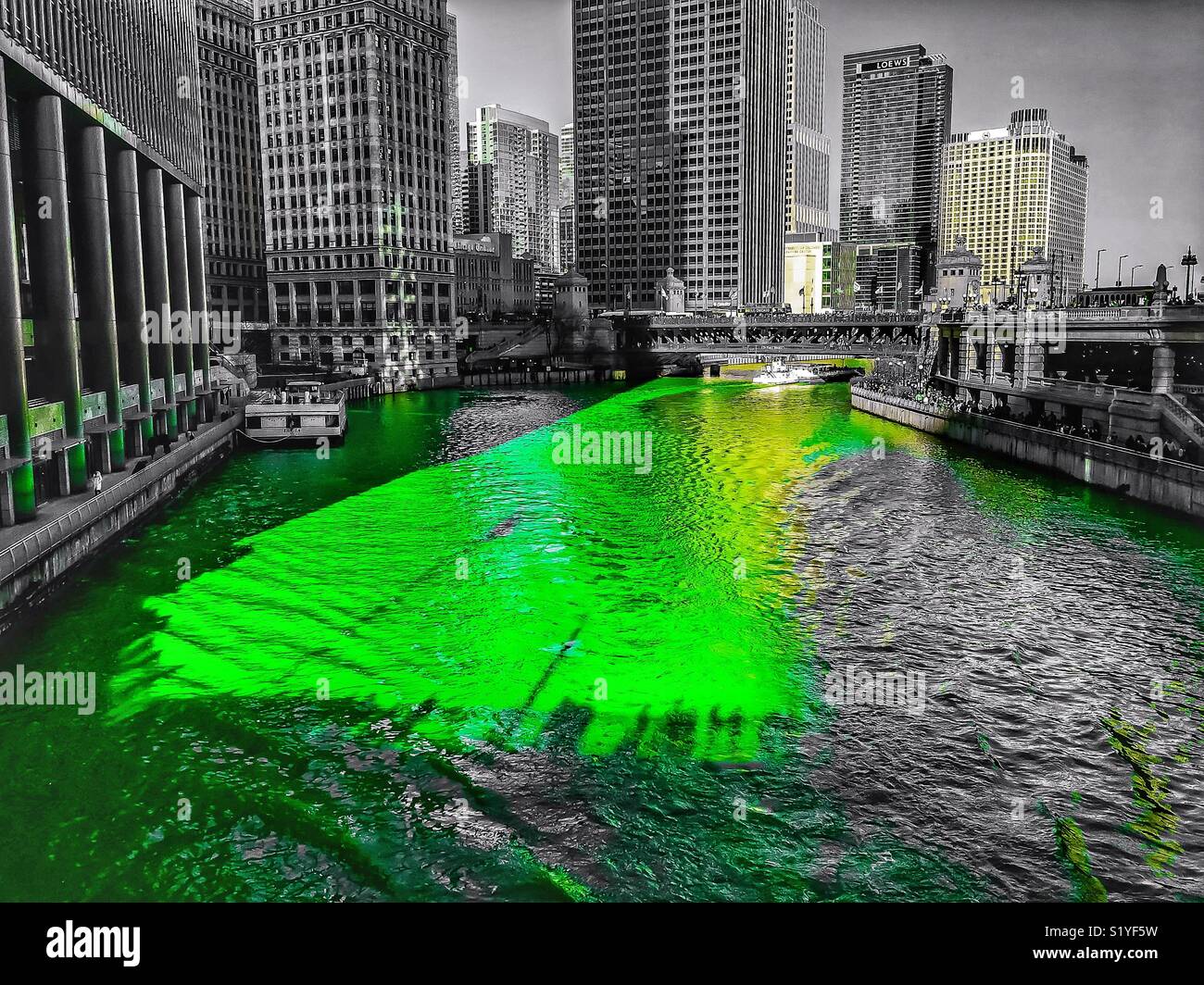 Chicago River ist gefärbt grün für St. Patrick's Day. Schatten der Brücke holding Menschenmassen und Flags sind auf dem Wasser Oberfläche bedruckt. Stockfoto