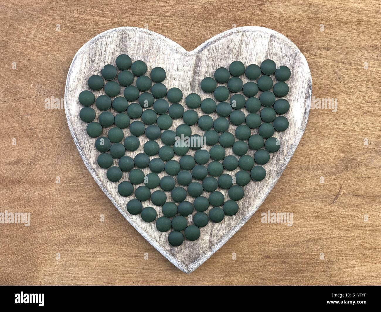 Spirulina Tabletten auf einer hölzernen Herz Symbol der Gesundheit Stockfoto