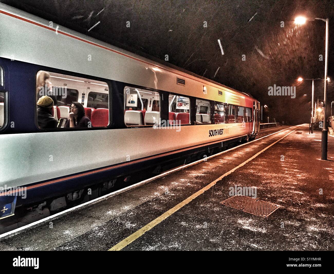 South West Train am Bahnhof Sherborne bei Sonnenaufgang, mit Pendlern im Zug, Salzschrot auf dem Bahnsteig und Schneefall, Sherborne, Dorset, England - Smartphone-aufgenommenes Stockfoto