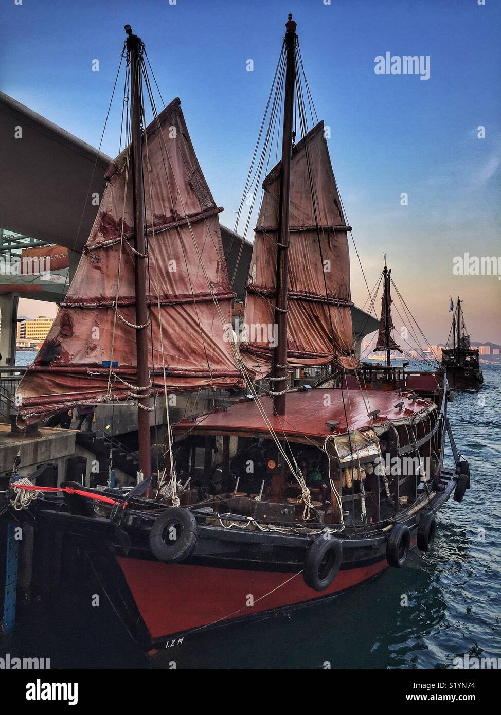 Die "Uk Ling", ein Nachbau der chinesischen Dschunke, für Sightseeing Kreuzfahrten auf den Victoria Harbour, Kommissionierung bis Touristen am Pier 9, Central, Hong Kong Insel bei Sonnenuntergang - Smartphone-aufgenommenes Stockfoto