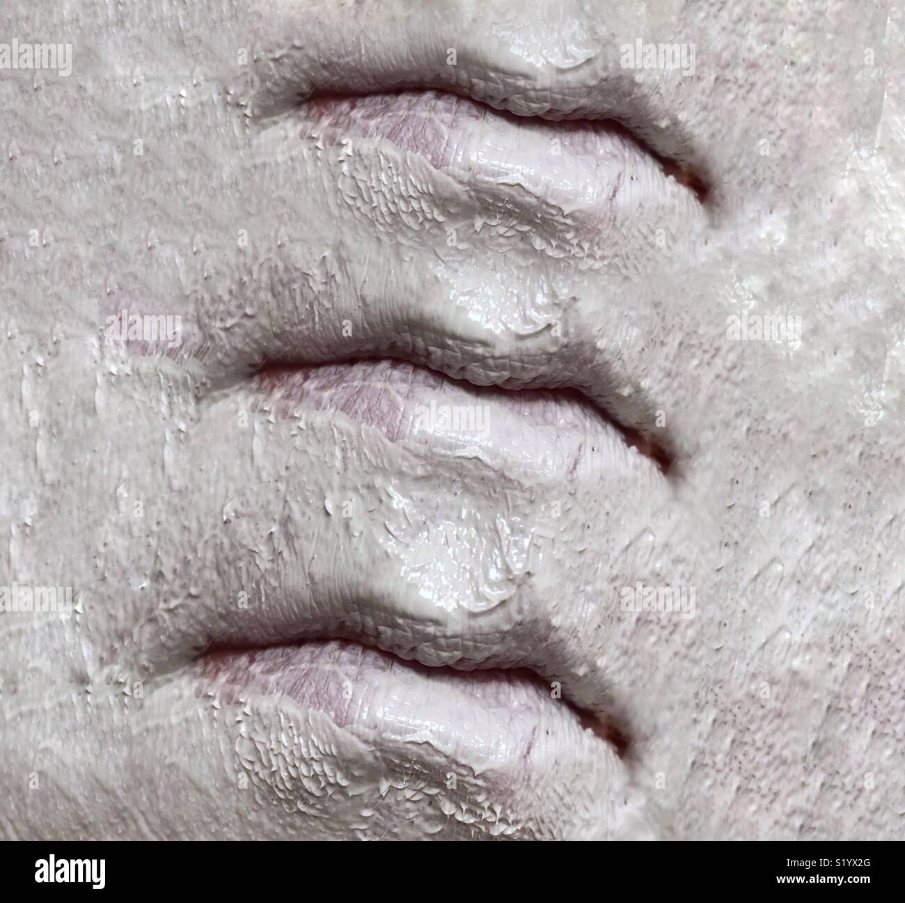 Ein abstraktes Bild von drei Sets von Lippen auf ein Gesicht in einem weißen Ton Schlamm Maske abgedeckt Stockfoto