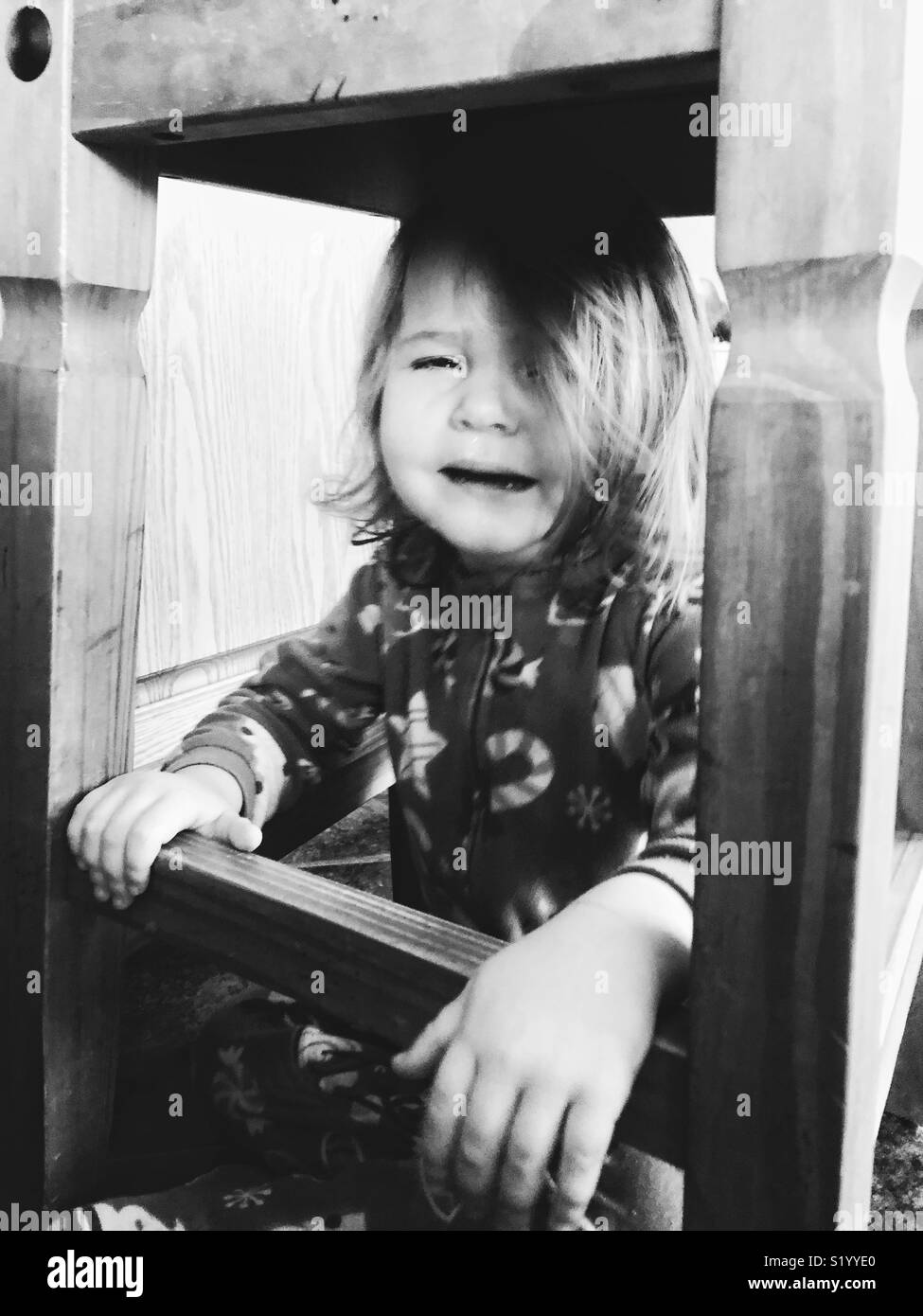 Schwarz-weiß Bild von Kleinkind Mädchen unter einem hölzernen Hocker schreien Stockfoto