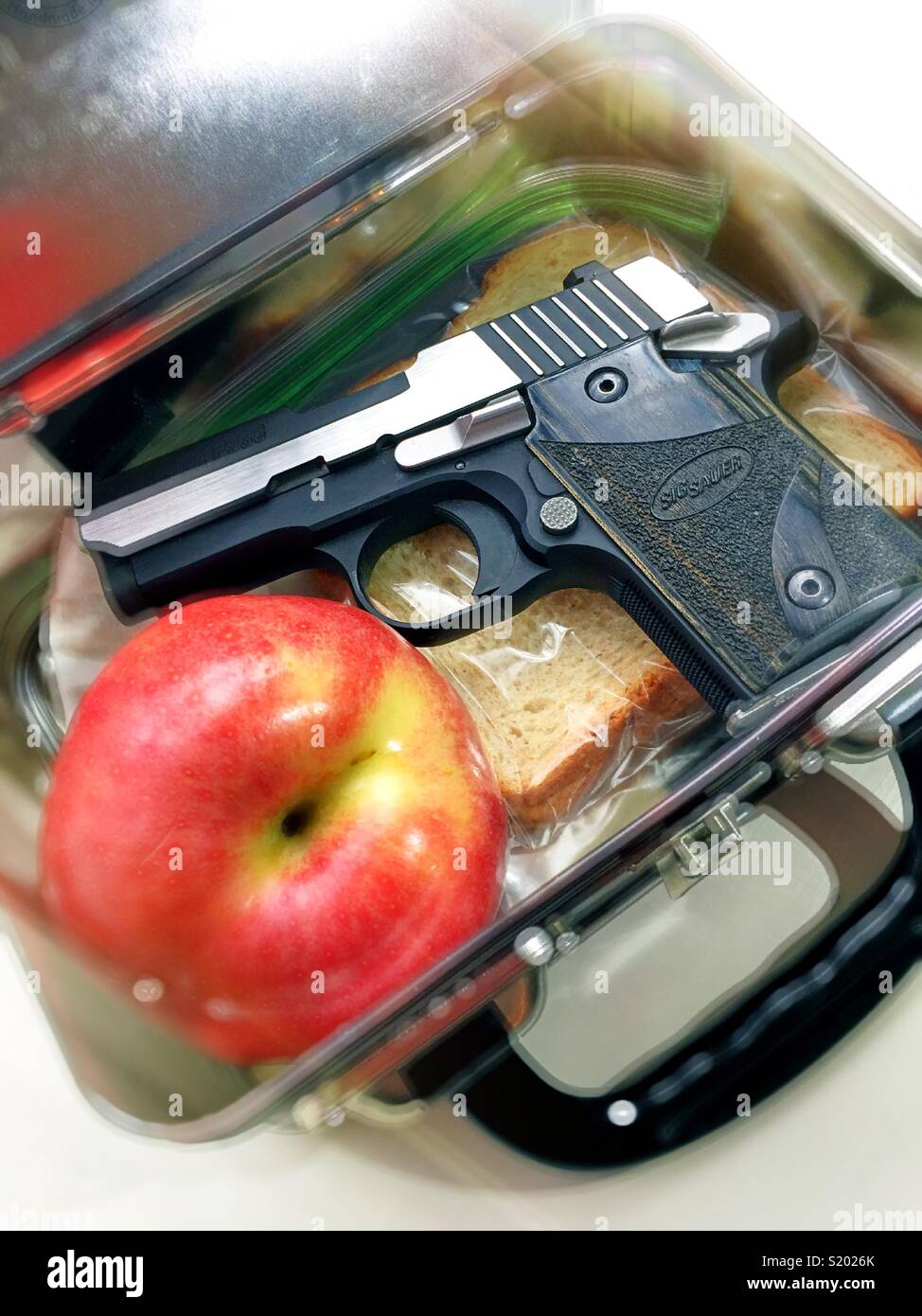 Brotdose mit einem Kind Mittagessen gefüllt und mit einem kleinen automatischen Pistole, United States - Smartphone-aufgenommenes Stockfoto