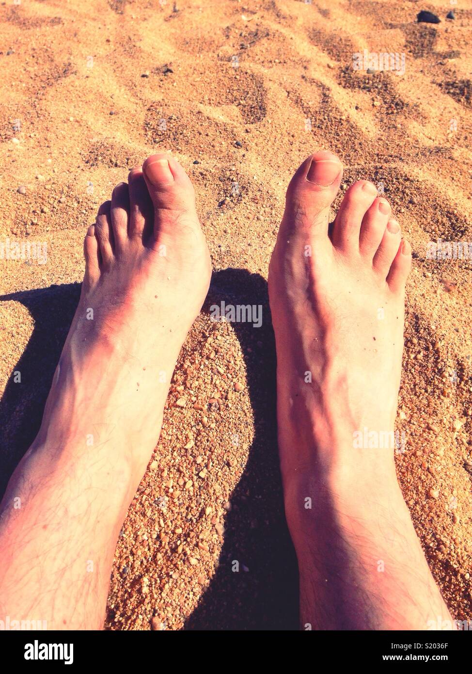 Männliche Füße an einem Sandstrand. Stockfoto