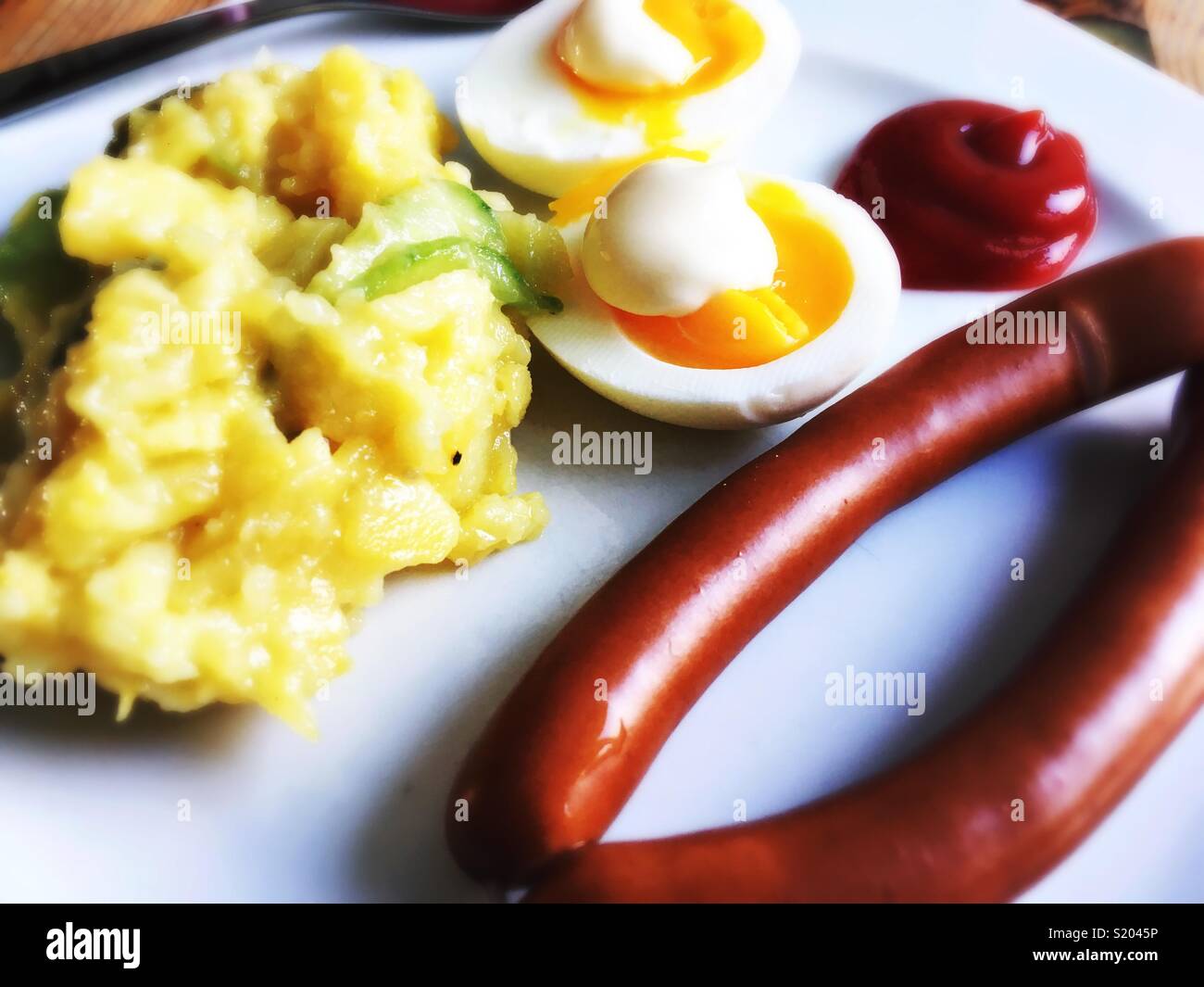 Ein paar Wiener Würstchen, Eier, Mayonnaise, Kartoffelsalat und Ketchup auf einem weißen Teller Stockfoto