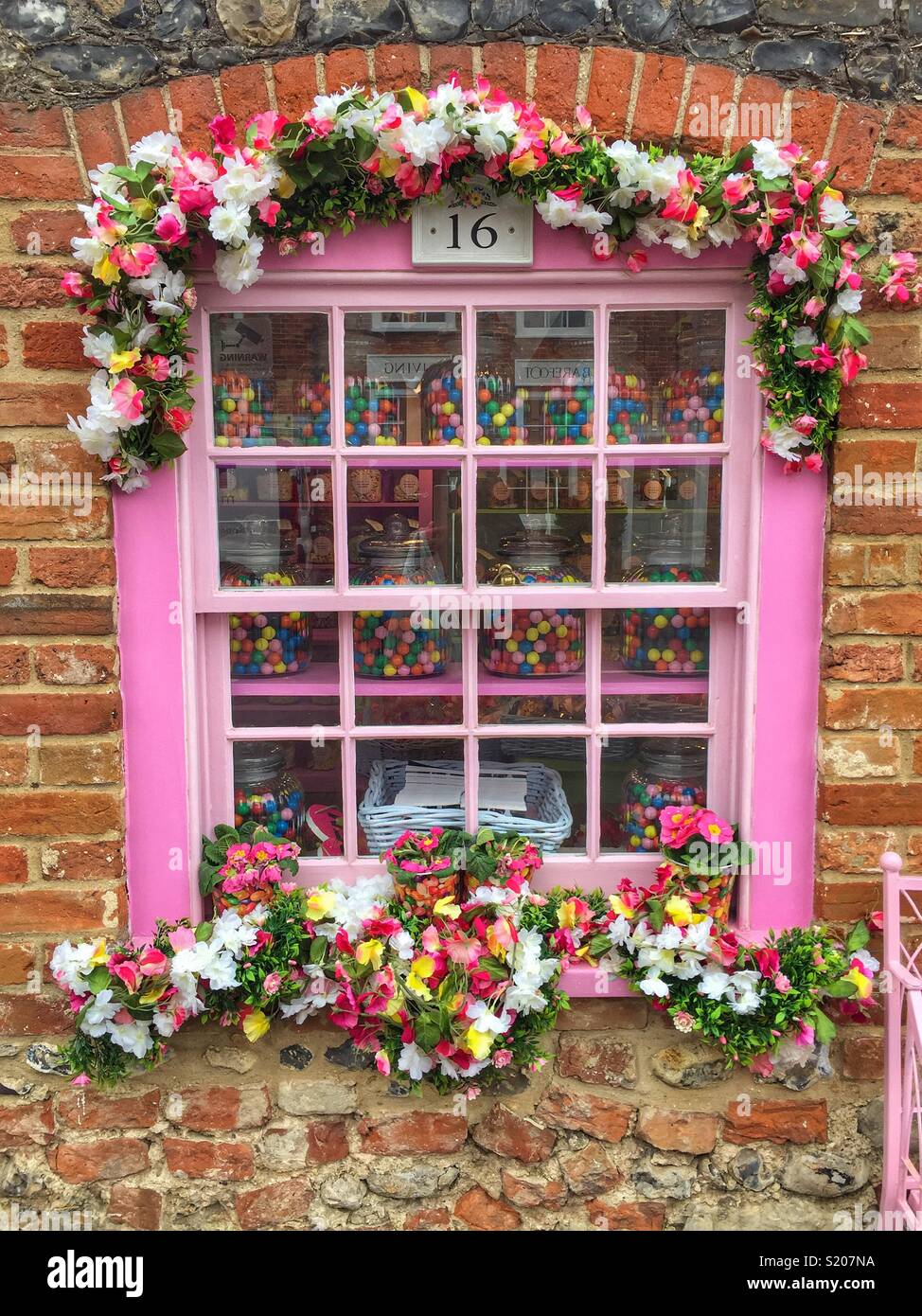 Die hübschen rosafarbenen Fenster einer urigen Hütte mit bunten Blumen geschmückt Stockfoto