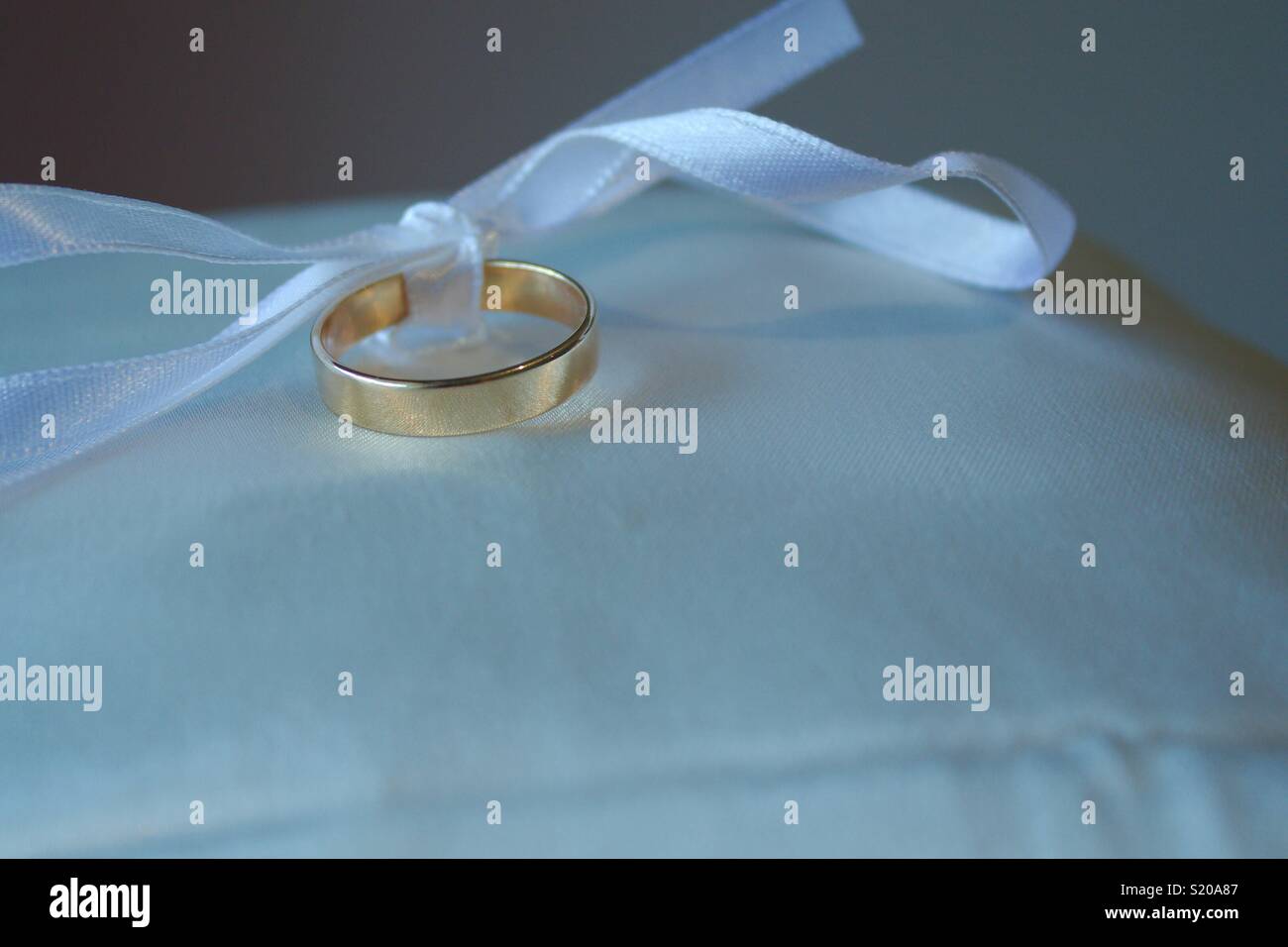 Eine goldene Hochzeit Ring sitzt auf einem ringträger Kissen mit, eine weisse Schleife in einer Schleife gebunden. Stockfoto