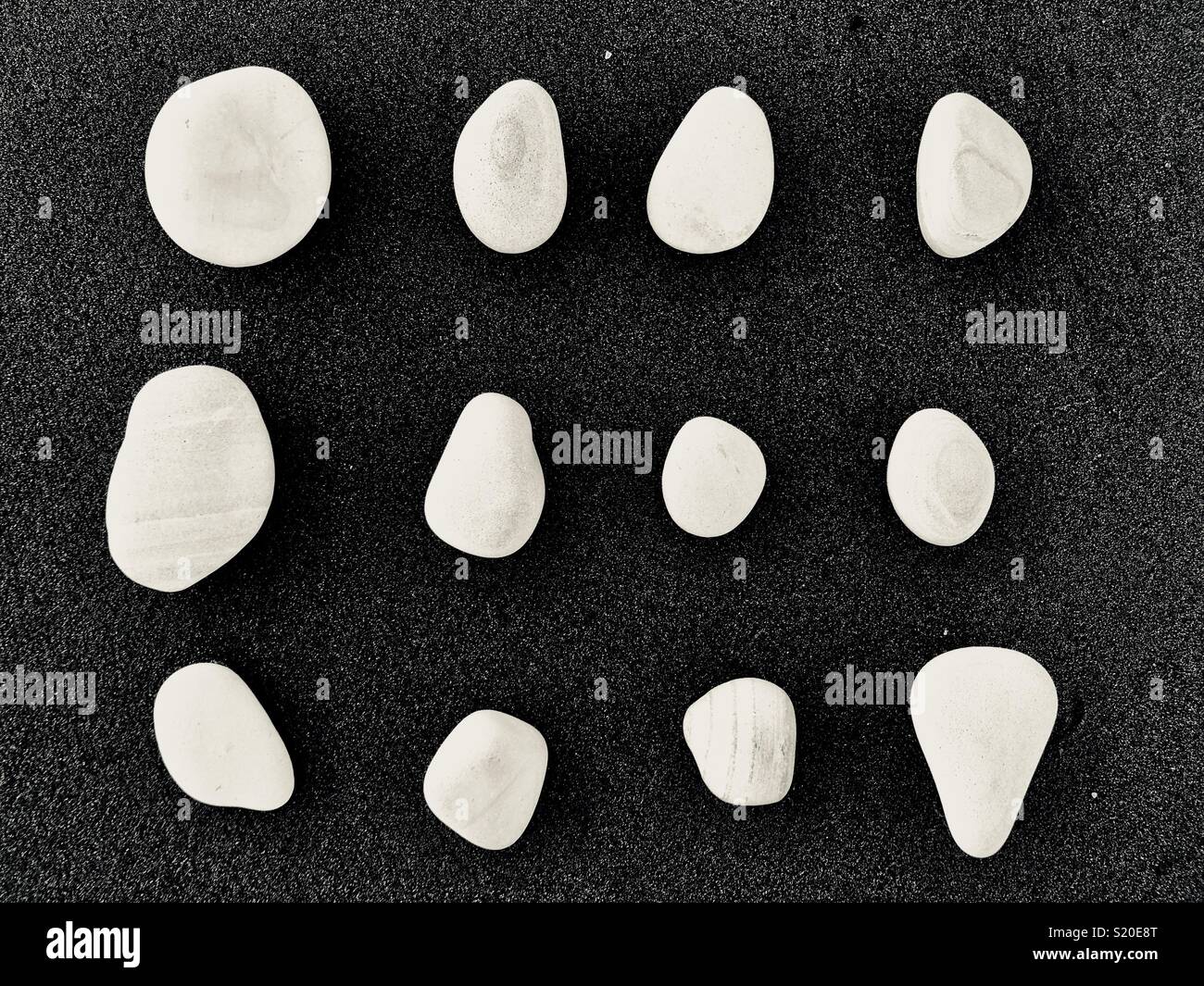 Steine weiß auf schwarzem Sand - Smartphone-aufgenommenes Stockfoto