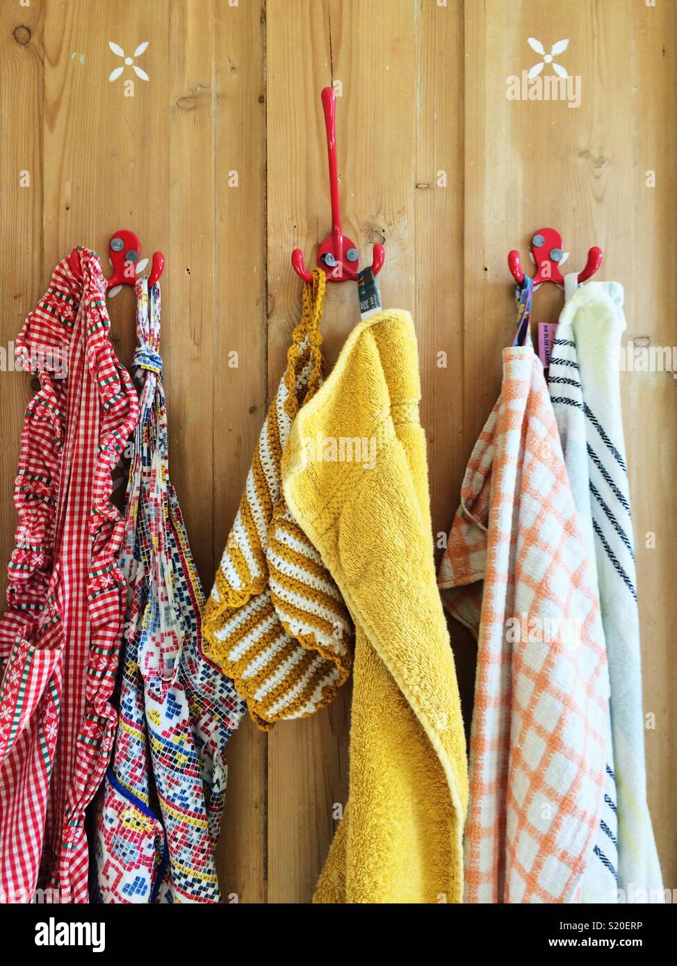 Schürzen und Handtücher hängen auf der Rückseite der Holztür auf roten Haken Stockfoto