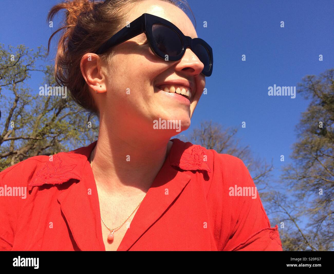 Portrait von Frau sucht sich Sonnenbrille und Red Top lächelnd Stockfoto