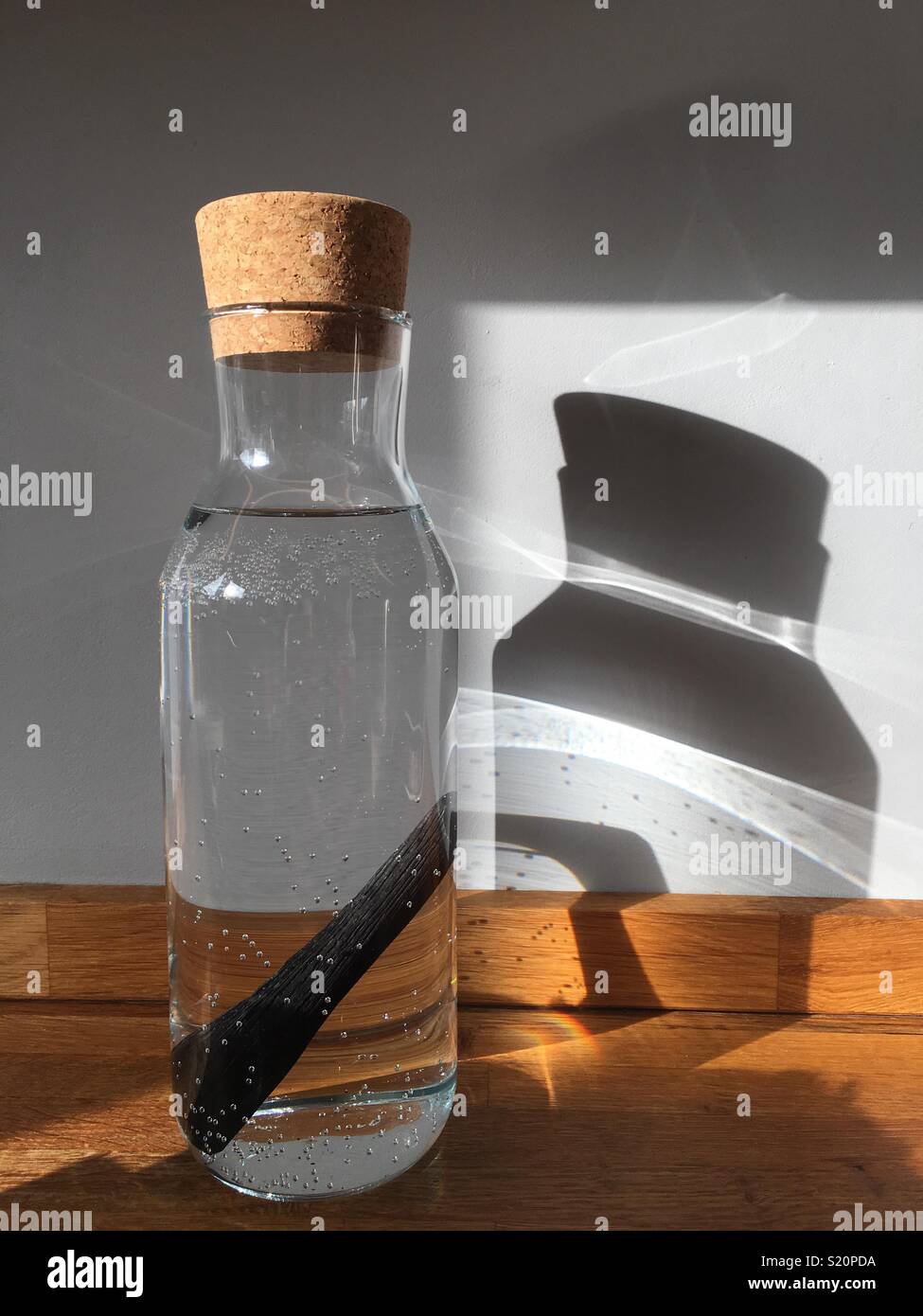 Einfache Glas Krug mit Wasser mit Aktivkohle stick Wasser zu reinigen, Sun durch interessante Muster an der Wand scheint. Stockfoto