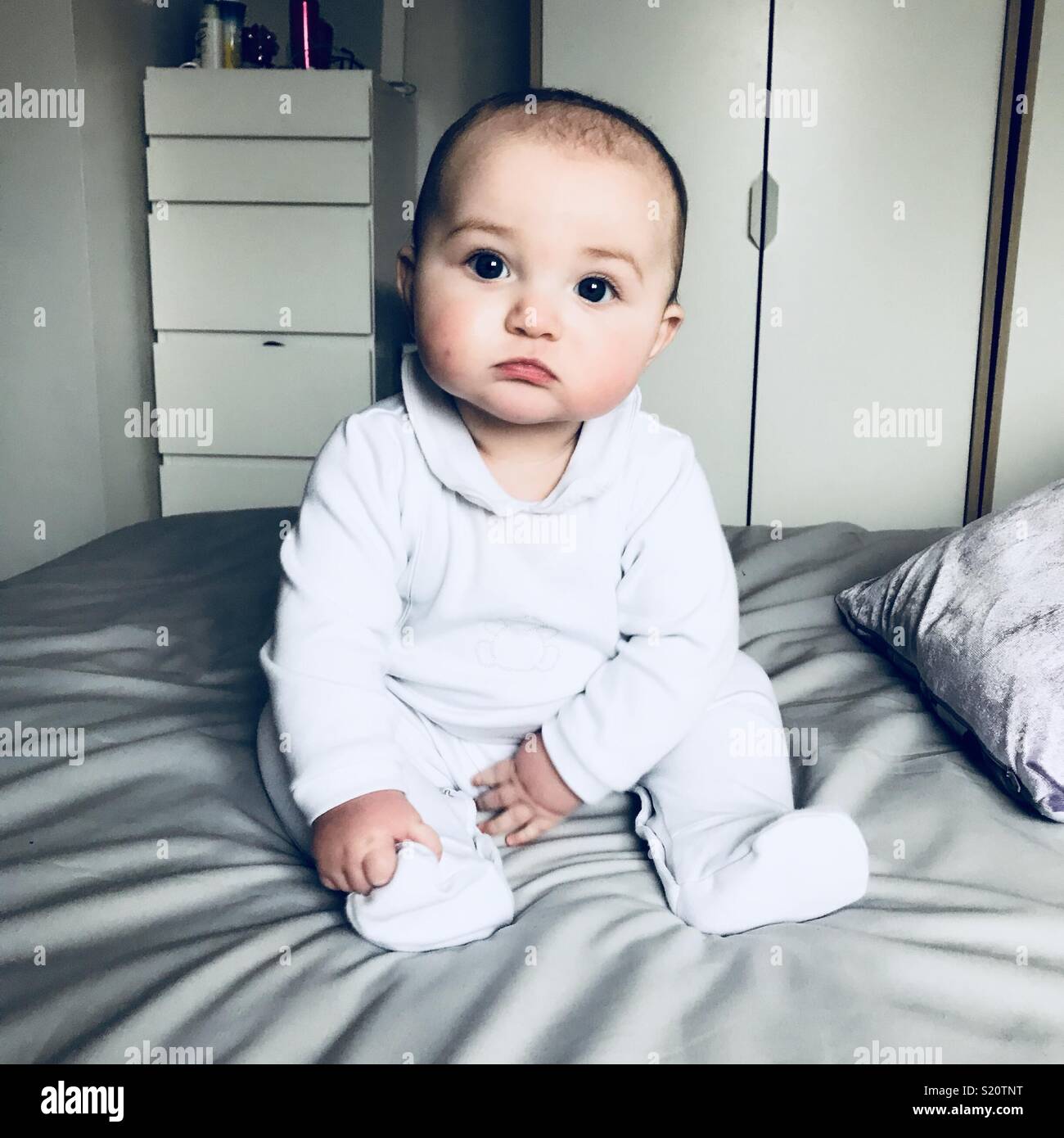 Baby in weiß Romper sitzen auf einem Bett. Stockfoto