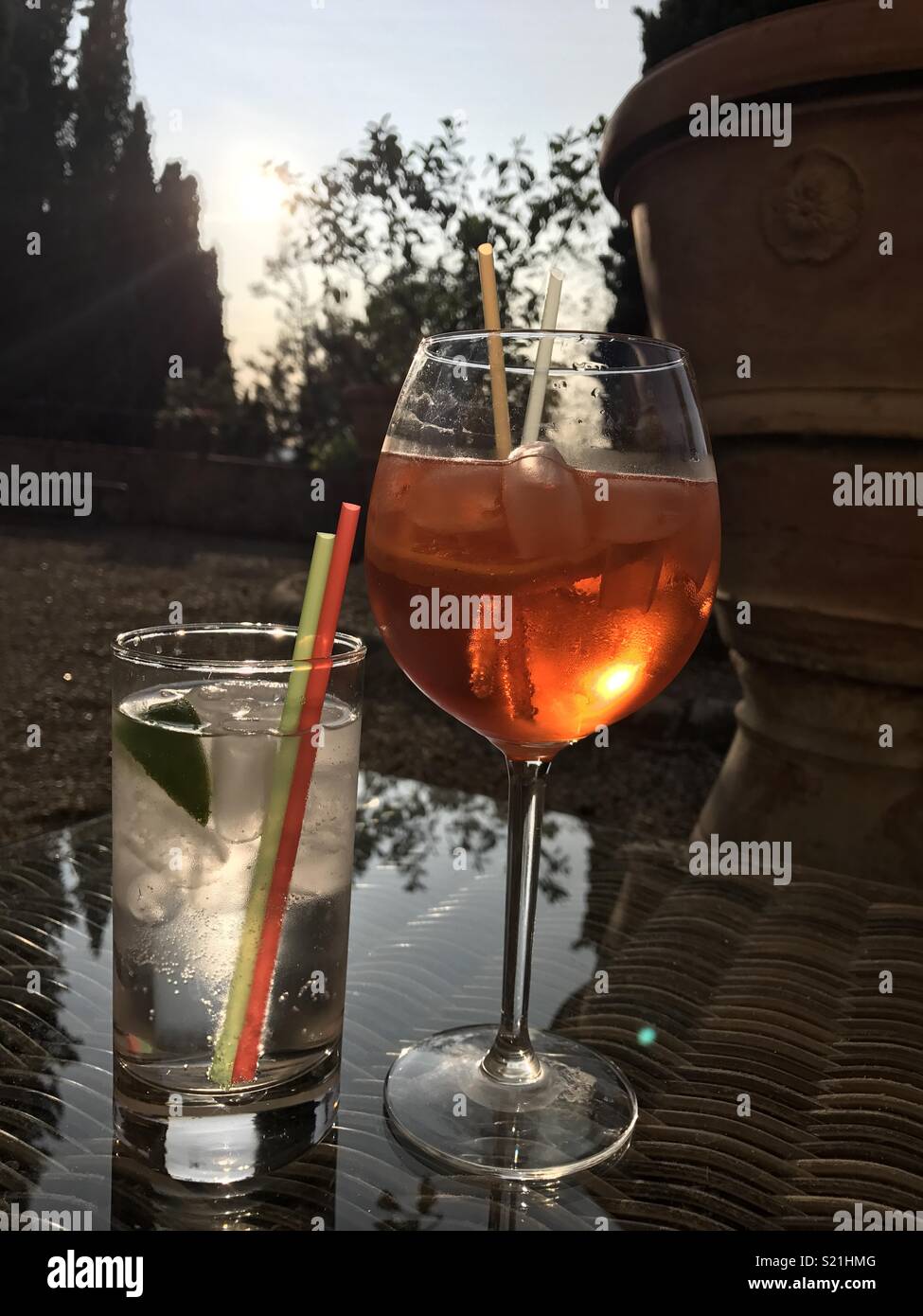 Urlaub am Abend Getränke im Freien in der Sonne verblassen Sie und Ihn Getränke mit Eiswürfeln und strohhalmen auf einem Glas Tisch im Garten Stockfoto