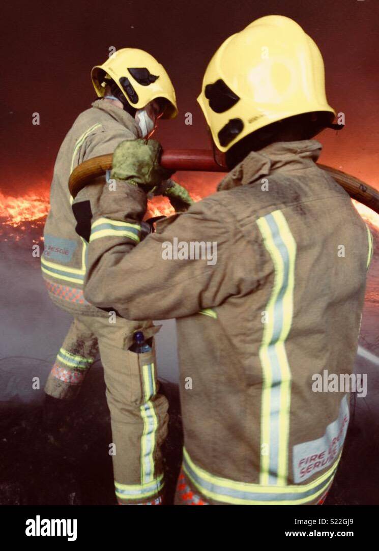 Zwei Feuerwehrmänner arbeiten zusammen, um ein Feuer zu setzen Stockfoto