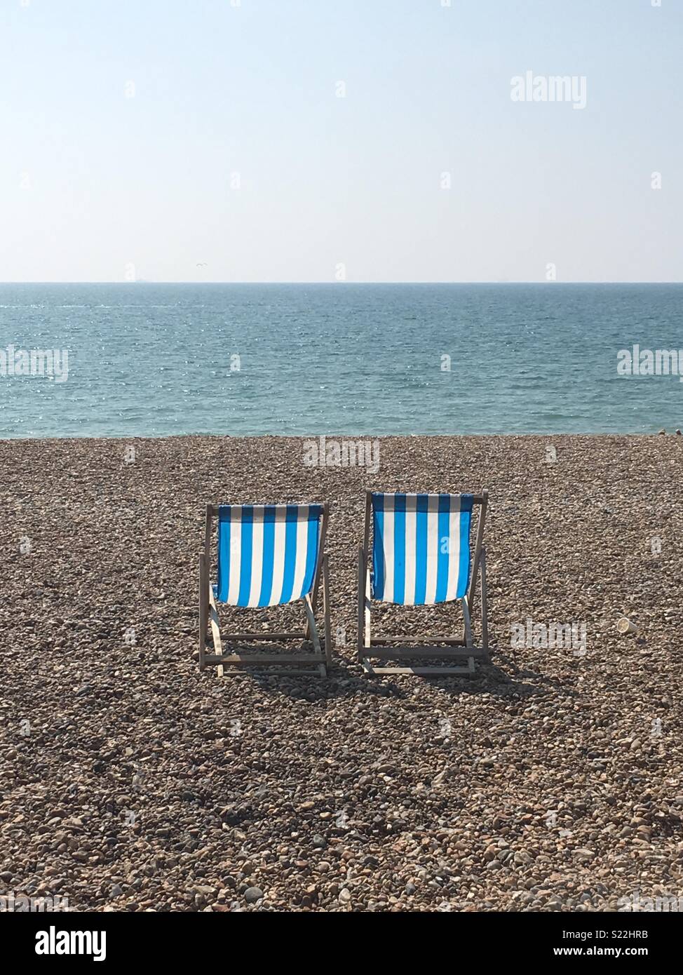 Zwei blau-weiß gestreifte Liegestühle am Brighton Beach, Großbritannien - eine typische englische Seeszene. Stockfoto