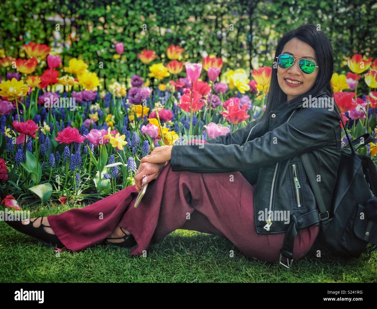 Eine Dame sitzt auf dem Boden und posiert für ein Foto vor einem blumenbeet der Tulpen. Stockfoto