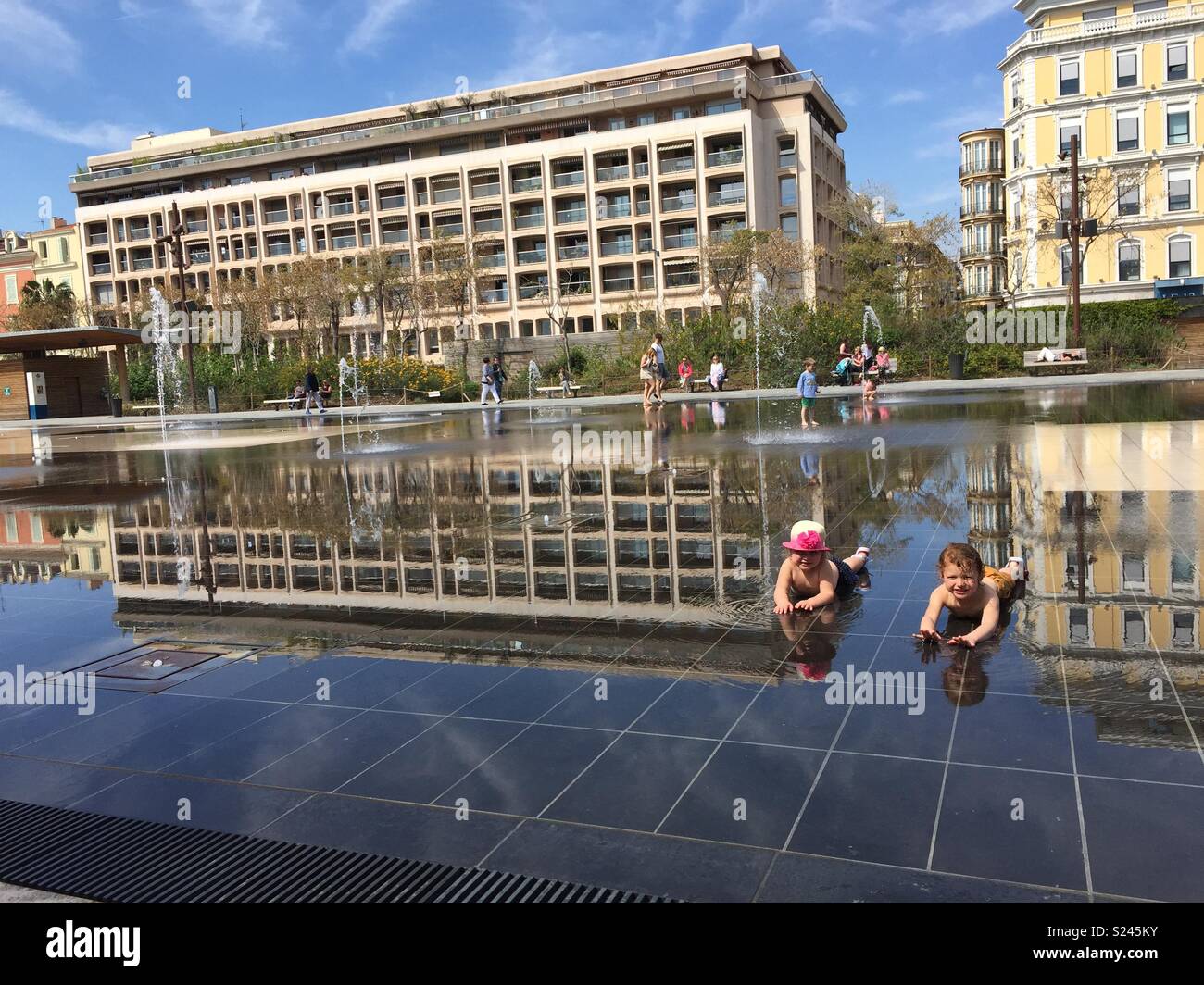 Schwestern spielen in einem Springbrunnen in Nizza, das Spiegelbild im Wasser ist atemberaubend Stockfoto