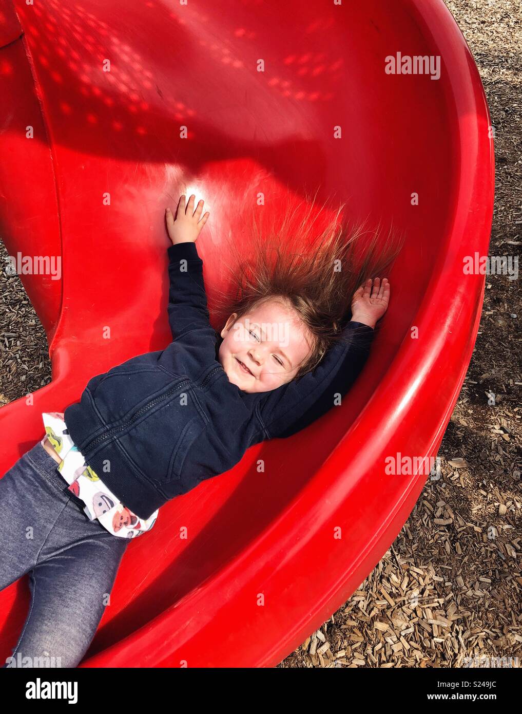 Aktion Bild von Toddler girl herunter rutscht, rote Folie mit Armen und Haaren bis klemmt Stockfoto