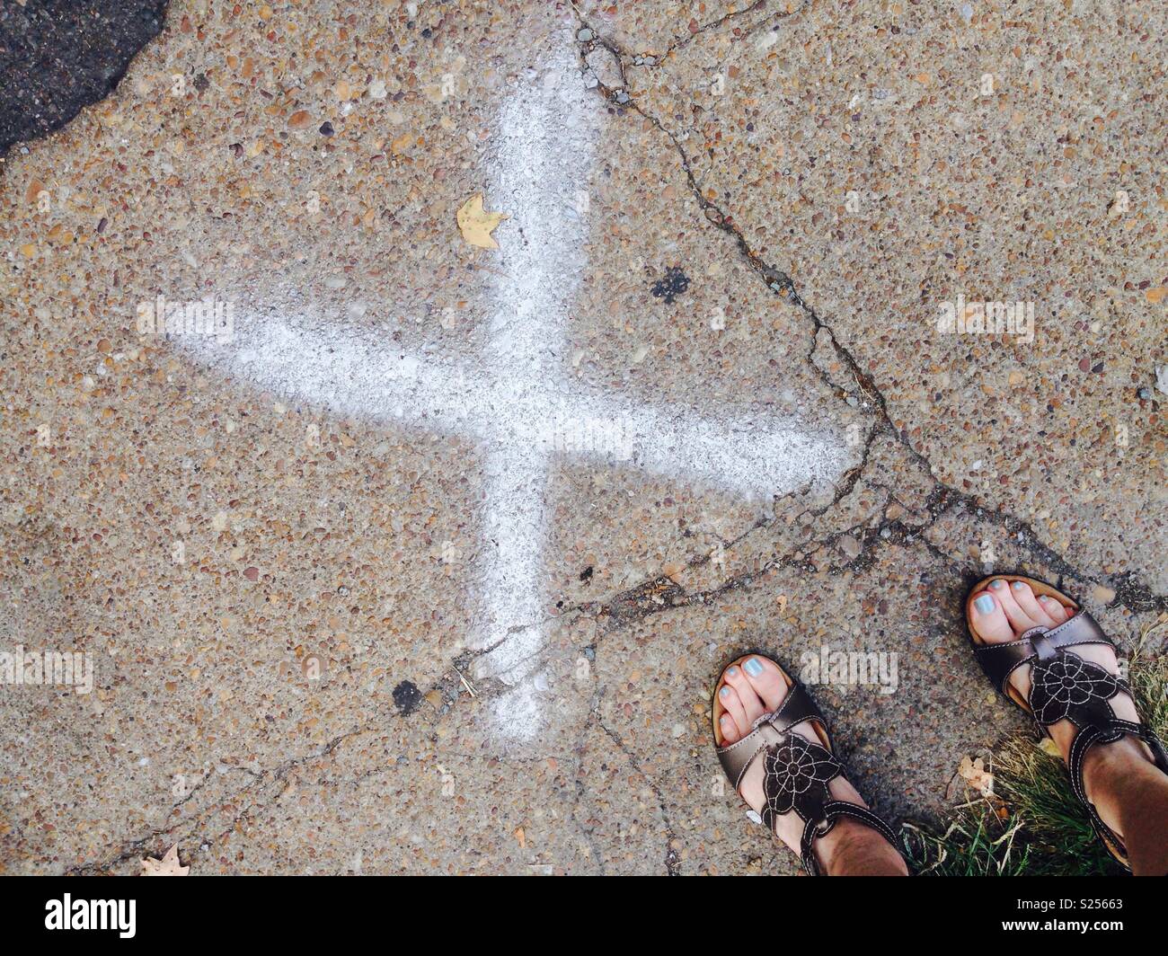 X markiert den Punkt. Füße der Frau zu einem großen X Mark auf einem Bürgersteig. Stockfoto
