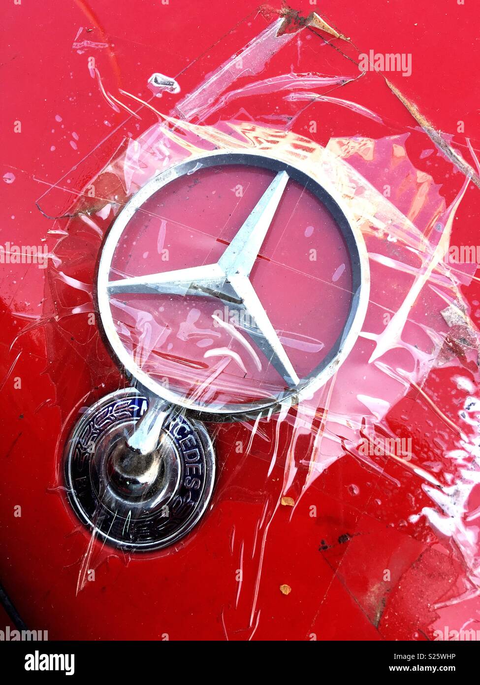 Eine gebrochene Mercedes Benz Star Logo auf der Motorhaube von einem roten Daimler, mit durchsichtigem Klebeband befestigt Stockfoto