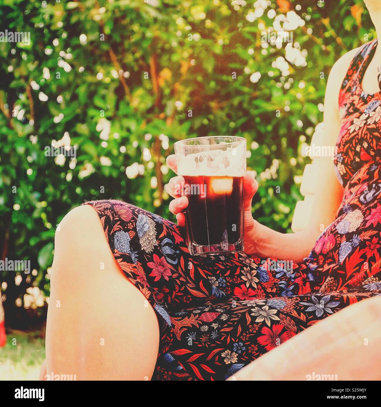 Frau mit einem Drink im Freien an einem sonnigen Tag - Smartphone-aufgenommenes Stockfoto