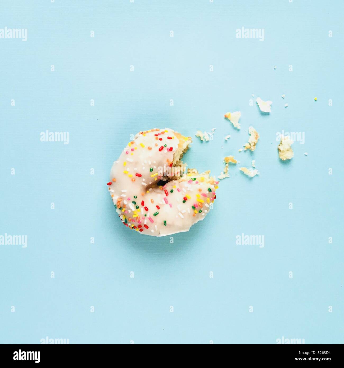 Ein weißer Sprühregen Donut mit einem Bissen aus auf einem blauen Hintergrund. Stockfoto