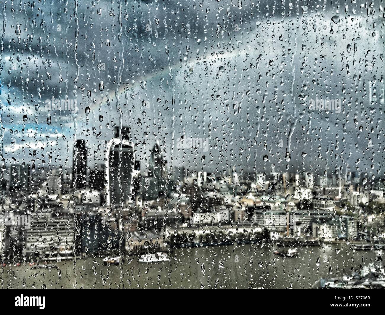 Regen auf dem Fenster der Shard, London, UK, über die Themse in Richtung Fenchurch Street und über die Stadt. Ein Regenbogen der Himmel leuchtet wie die Sonne durch Brüche, beleuchtet die Stadt unten. - Smartphone-aufgenommenes Stockfoto