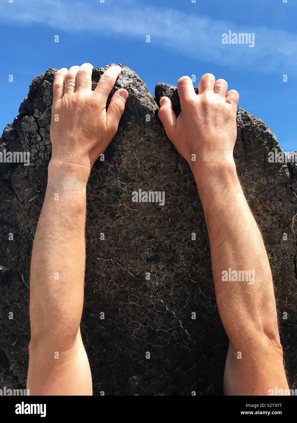 Ein paar menschliche Hände und Arme auf einen rauen Felswand festhalten Stockfoto