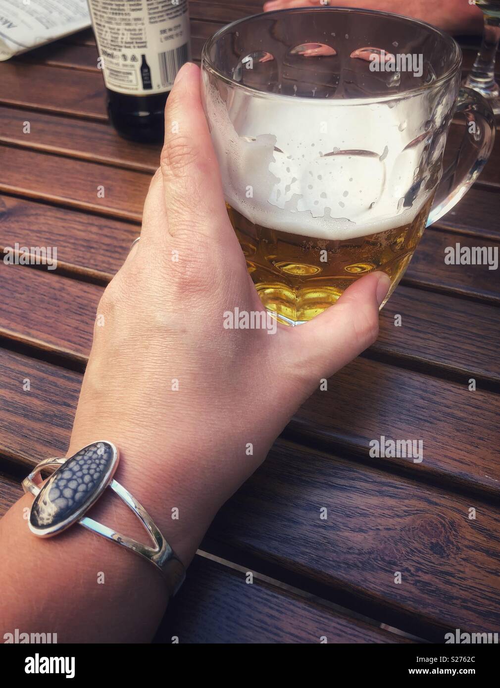 Frau mit einem halb betrunken Pint Bier in einem altmodischen pint Topf während des Sitzens mit einem hölzernen Tisch. Stockfoto